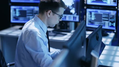 In Monitoring Room System Engineers Working at Their Workstation. Multiple Screens Display Various