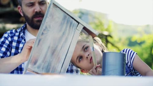 Père avec une petite fille à l'extérieur, peignant un nichoir en bois