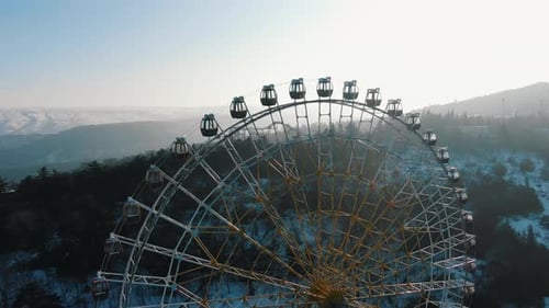 Stationary Ferris Wheel Rests on a Snowy Mountain Soaking in Bright Sunlight Beneath a Clear Blue