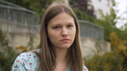 A Beautiful Young Caucasian Woman Looks Seriously at the Camera a Building in the Background