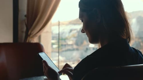 Closeup Beautiful Woman Using Social Media and Smiling at Smartphone in Cafe with Beautiful View