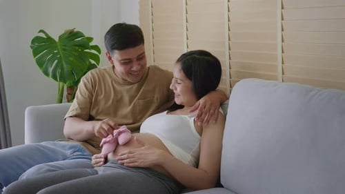 Pregnant Couple with Baby Shoes Smiling on Couch