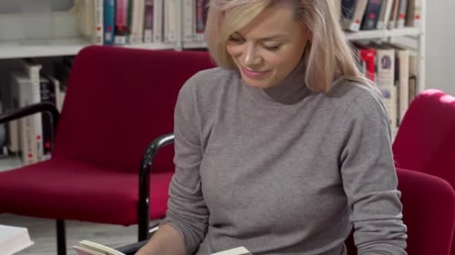 Stunning Woman Smiling to the Camera While Reading at College Library