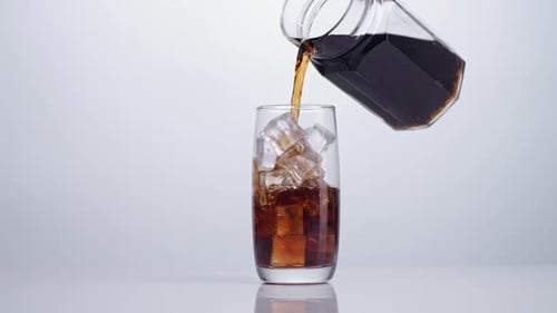 Fresh Cola Being Poured In To The Glass With Ice Cubes On White Background