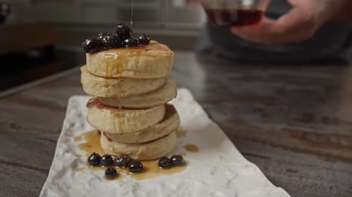 Ahornsirup wird auf Blaubeeren und einen Stapel amerikanischer Pfannkuchen gegossen.