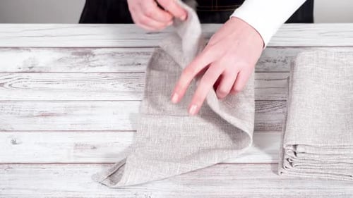 Woman Folding Linen Napkin on Rustic Wood Table