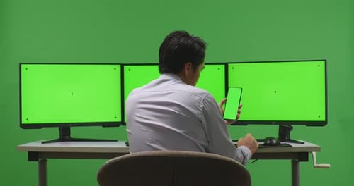 Man Using Mobile Phone And Multiple Monitor With Mock Up Green Screen In Green Screen Studio