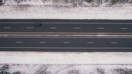 Aerial View of the Movement of Cars on the Highway Among Snowcovered Fields and Forest