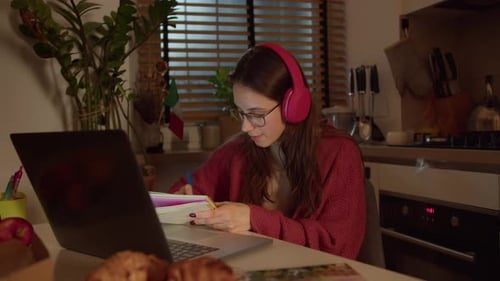 A Confident Brunette Girl in Red Wireless Headphones and a Sweater Studies Foreign Languages Taking