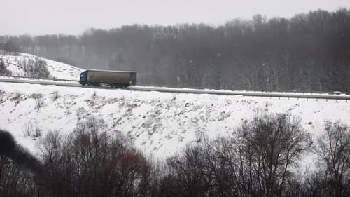 Truck Driving on Winter Road Surrounded Forest in Snowfall