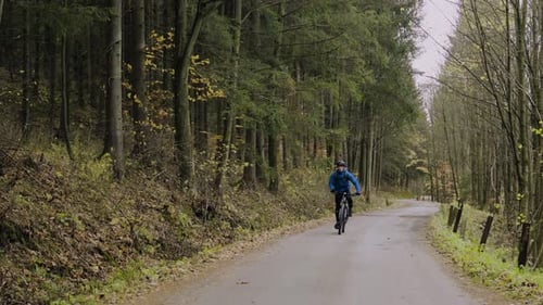 Young man rides bicycle along country road through beautiful autumn forest