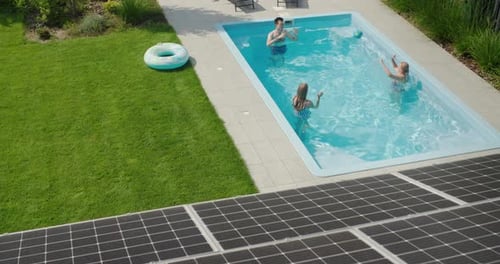 A Cheerful Family Plays in the Pool in the Foreground are Solar Power Panels on the Roof of Their