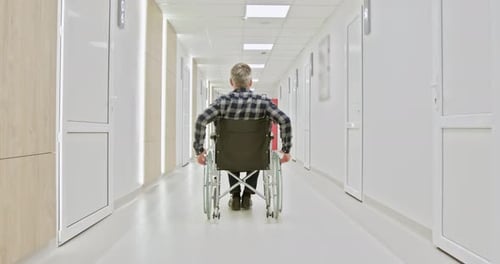 MiddleAged Man in Wheelchair Navigating Hospital Corridor