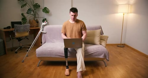 Man with Prosthetic Leg Using Laptop at Home