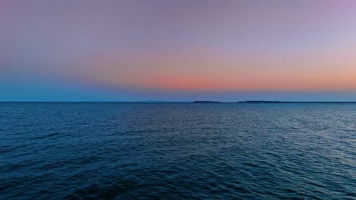 Footage over the vast blue seascape at sunset time. Beautiful blue pink sky at backdrop.