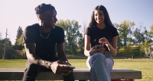 Teenage couple enjoying social media on smartphones in a sunny park