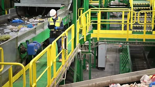 Worker Inspecting Waste on Conveyor Belt in Recycling Plant