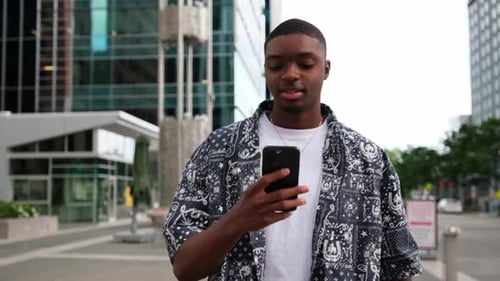 Stylish Young African American Man Focused on Smartphone in Vibrant City Ambiance