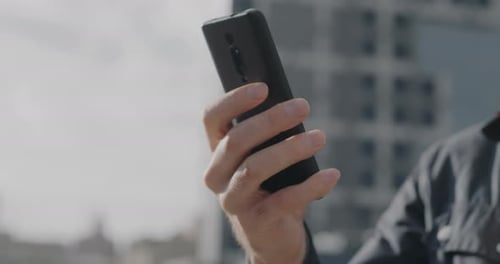 Closeup of Hand Holding Modern Smartphone While Businessman Using Mobile Phone Outside in City