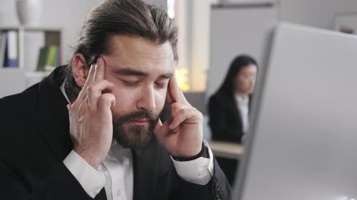 Bearded Man Massaging Temples in Office
