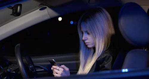 Woman Sitting In The Car Using Smartphone In The Dark. Woman Driver At Night.