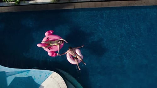 Couple Floating in Swimming Pool on Inflatables