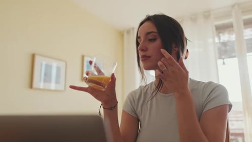 Woman Drinks Juice While Using Laptop at Home