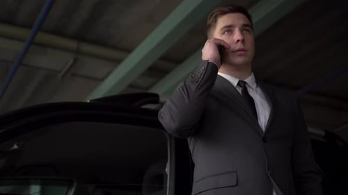 Businessman Speaks on the Phone Near the Car in the Parking Lot