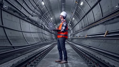 Full Body Side View Of Asian Male Engineer Working On A Laptop In Subway Tunnel