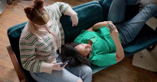 Two Young adult Female Friends looking at a Smartphone Together in a shared loft apartment on Sofa