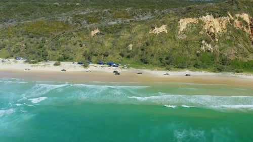 Aerial Drone Of Car Convoy Driving On Sandy Beach Beside Blue Ocean Waves