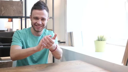 Man Smiling and Clapping at Table in Daylight