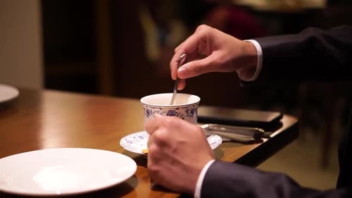 Man holds teaspoon in hand and mixes sugar in white ceramic cup