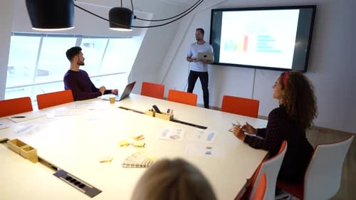 Smiling manager presents business growth charts to diverse team in office boardroom