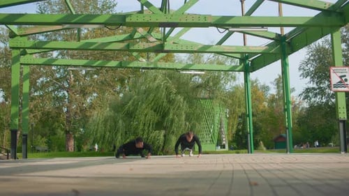 Park Pavilion Two Athletes Performing Pushups Morning Light on Green Steel Beams Tiled Ground