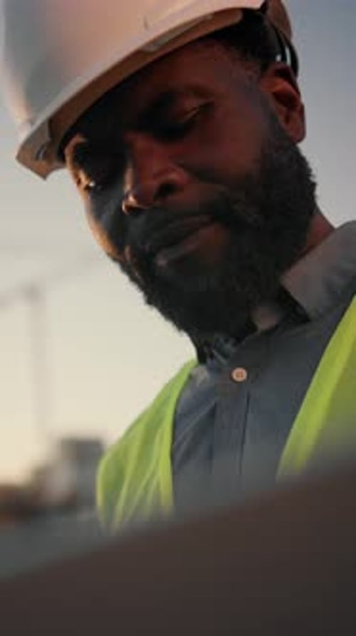 Bearded Foreman Viewing Drawings on Display of Modern Laptop in Construction Site Vertical Portrait