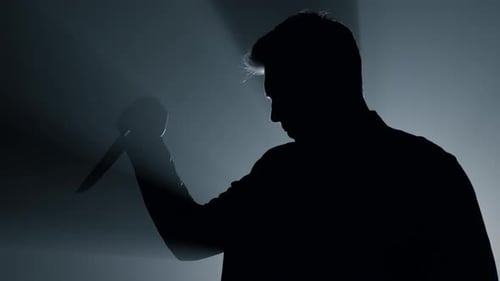 Silhouette of Aggressive Man Standing with Knife in Hand Indoors. Dangerous Criminal