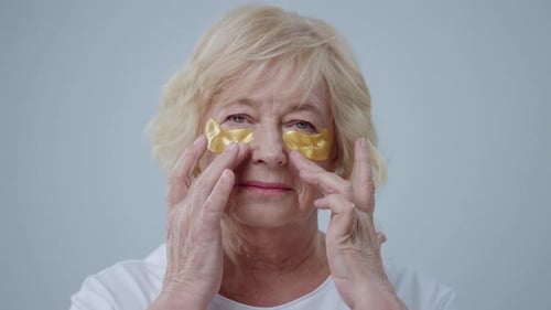 Senior Woman Applies Gold Eye Patches