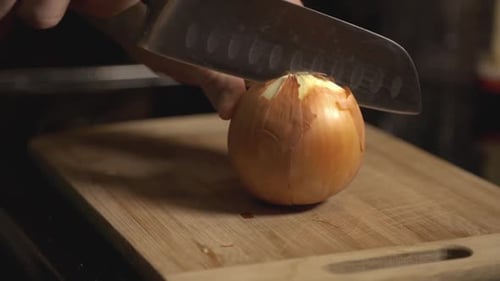 Slicing A Whole White Onion Using A Knife On Wooden Chopping Board. - closeup shot
