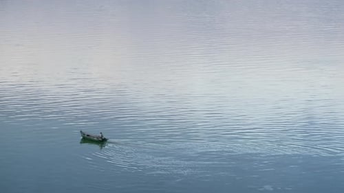 Fisherman sailing wooden boat on calm river at evening drone view