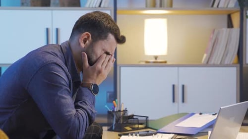 Tired Young Adult Working at Desk With Laptop