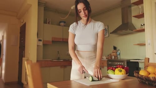 Woman Slicing Cucumber in Bright Kitchen
