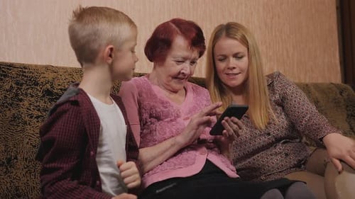 Family Gathers Around Mobile Phone on Sofa