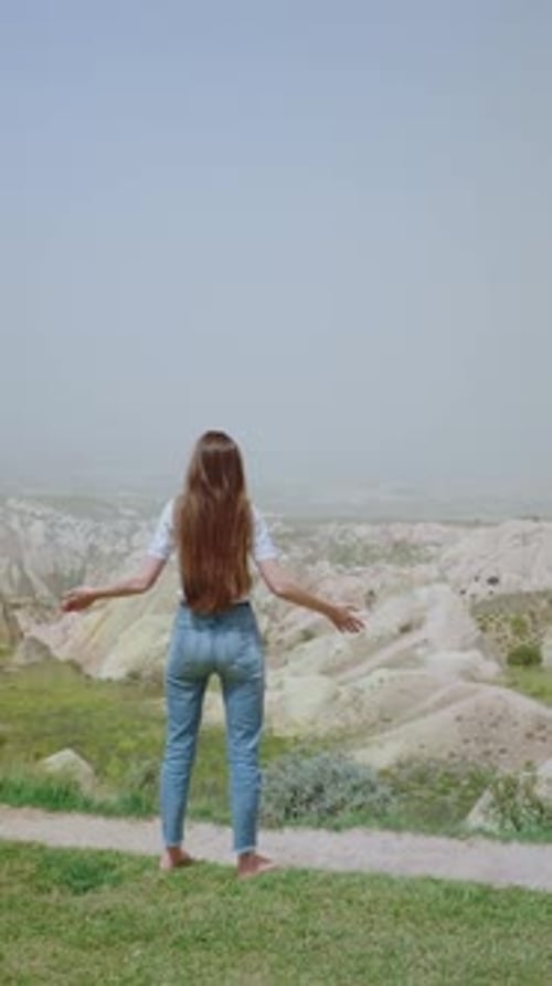 Rear View Unrecognizable Brunette Woman Standing with Arms Raised on Hillside