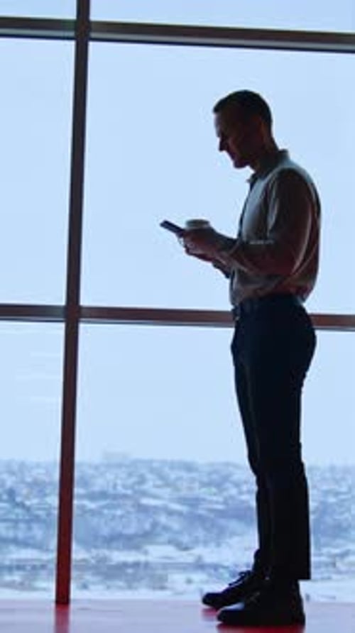 Office employee at the window with phone and white cup.