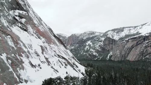 Aerial drone footage flying over Yosemite valley, towered by snowy granite cliffs in winter