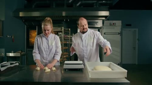 two bakers shape the raw dough before baking, cut it and roll it out on table professional kitchen