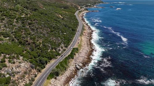 Panoramic drone clip of cars driving on coastal road with ocean and mountain views