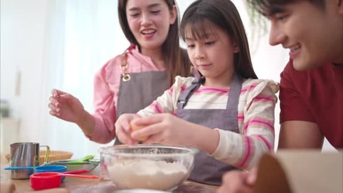 A family helping their daughter roll dough together in the kitchen, enjoying a fun baking moment