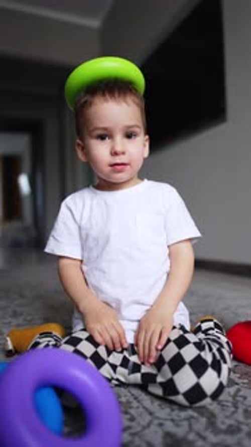 Un adorable bebé caucásico se sienta en el suelo con un detalle piramidal en la cabeza.